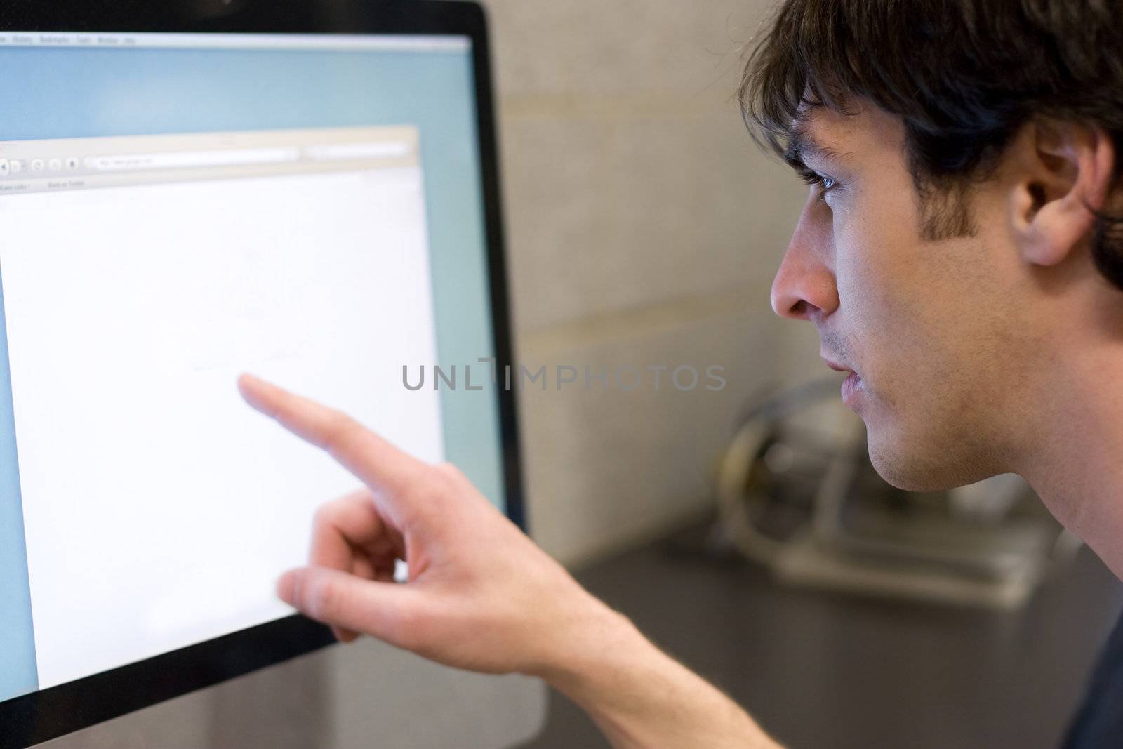 A young man pointing at a modern computer monitor lcd with copyspace.  Shallow depth of field with strongest focus on the face.