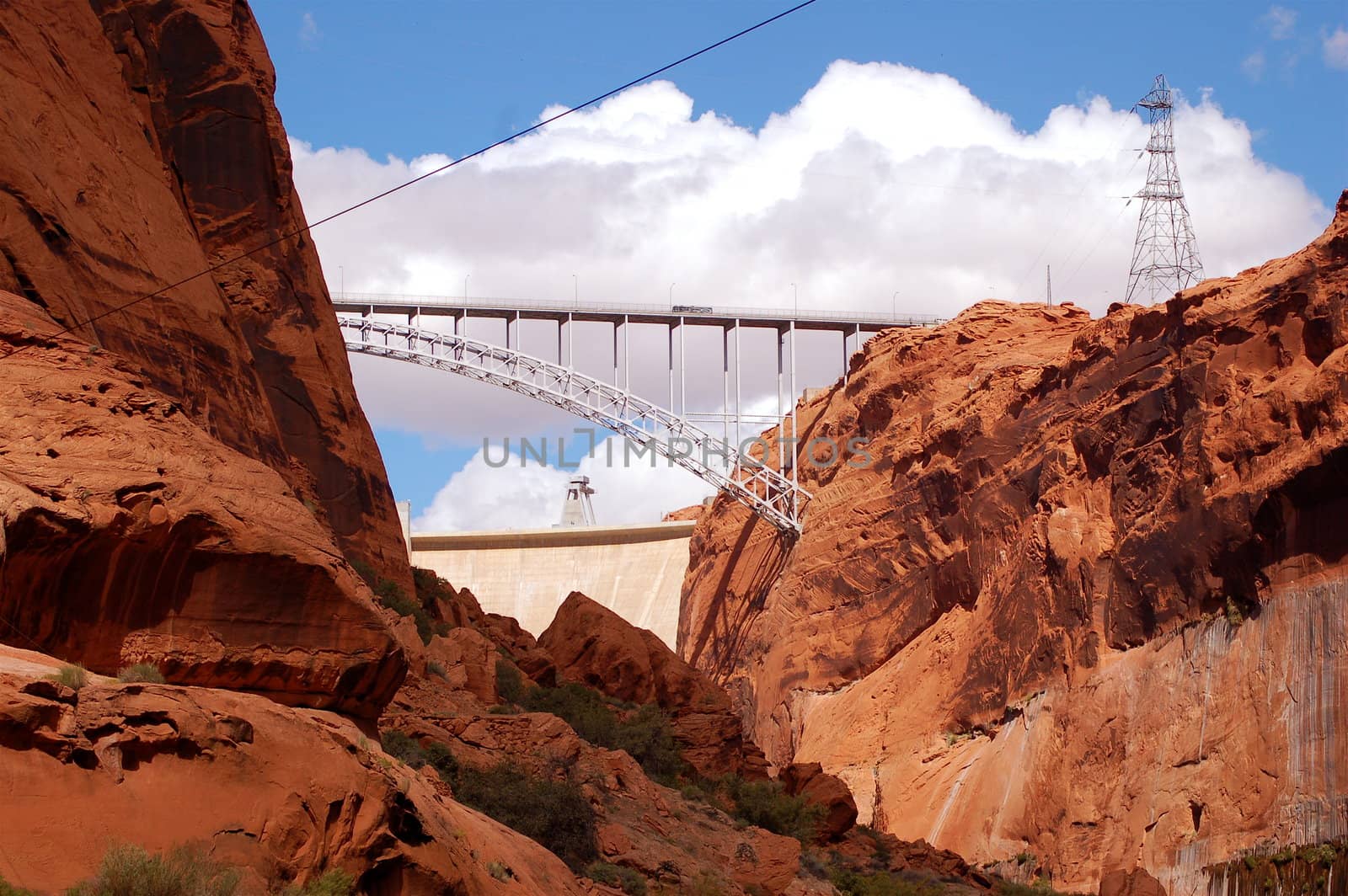 Glen Dam Bridge spanning the Colorado River, Arizona - with red rock either side and a bright blue sky filled with fluffy white clouds