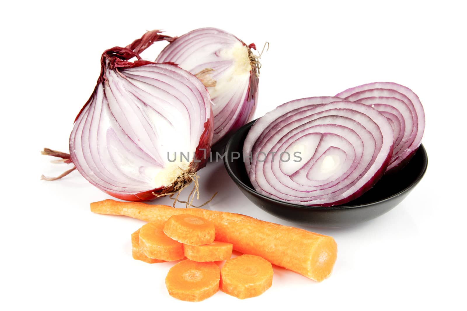 Raw red onion cut in half with slices in a dish and carrot on a reflective white background