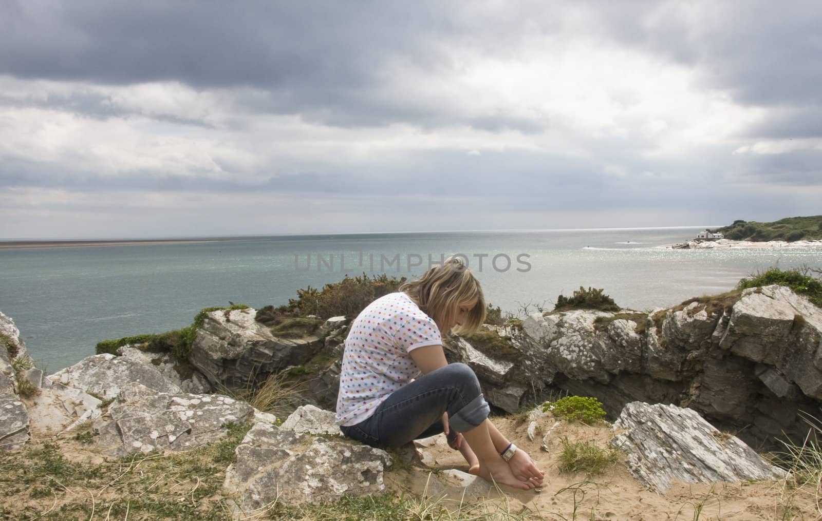 teenage girl sits on a rock getting the sand from between her toes.