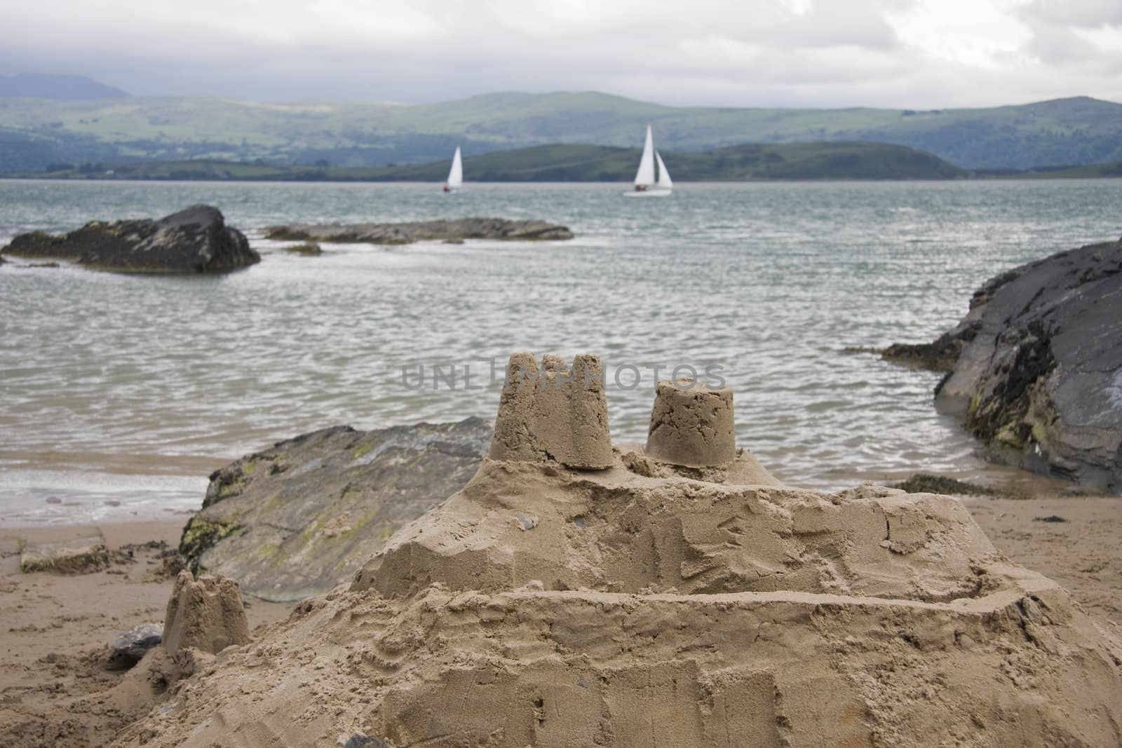 Sandcastle on the beach,with sea, yachts and mountains in the background.