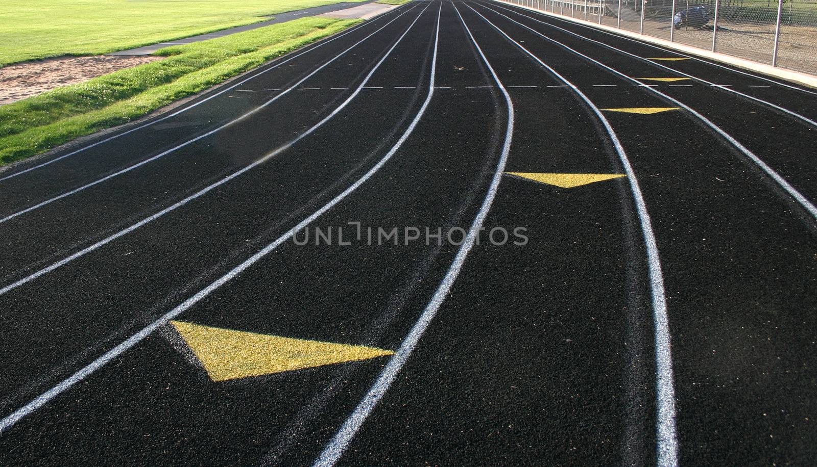 Black high school track showing lane markings with shadows of previous markings visible with arrows coming toward viewer.