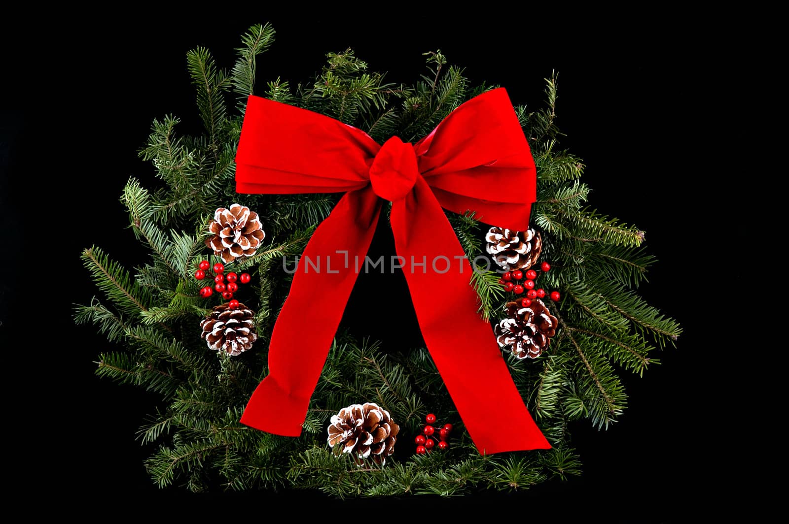 A Christmas wreath with red bow & decorative pine cones over black background.