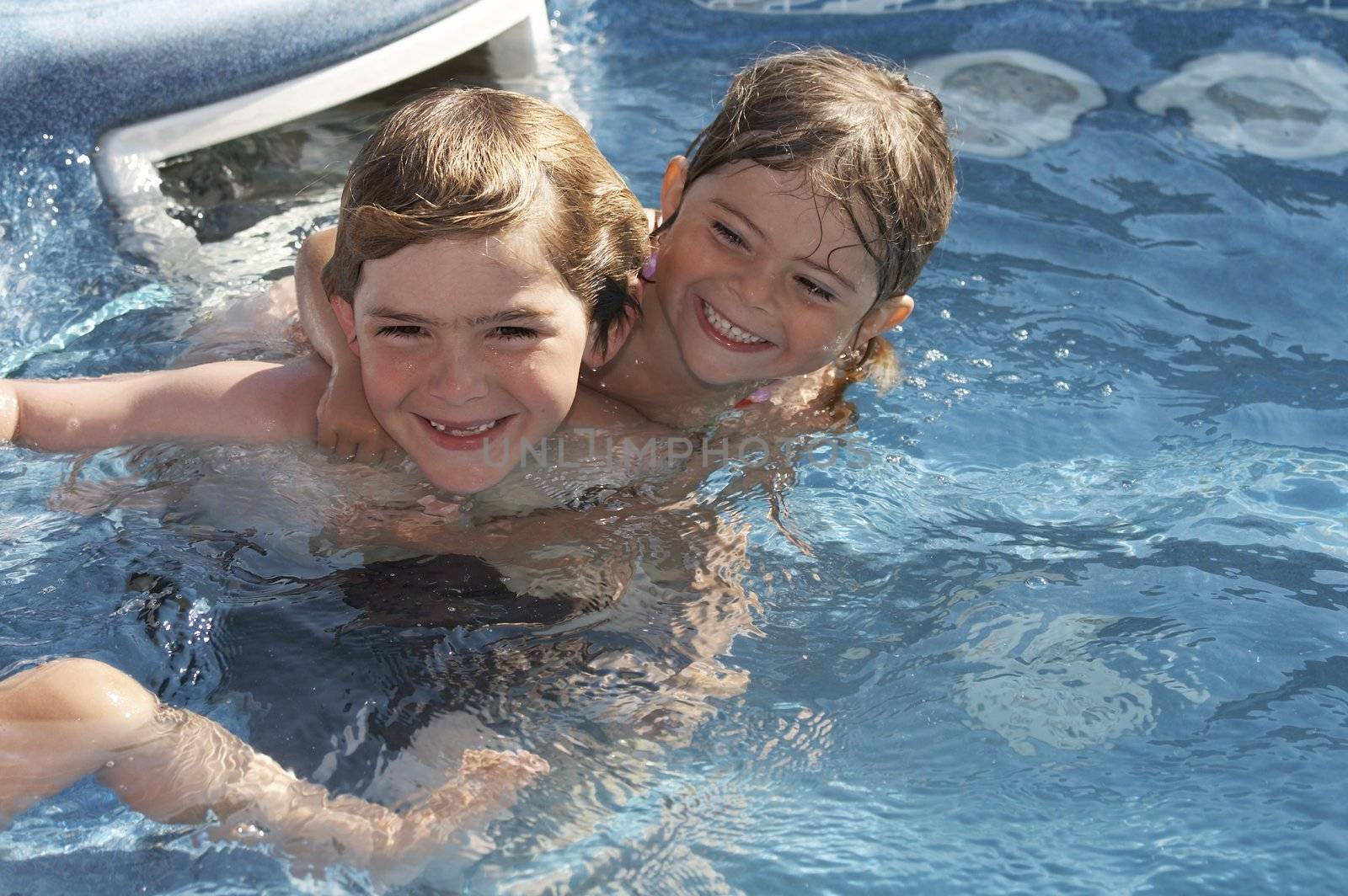 a cute little girl and boy in pool water during the summer