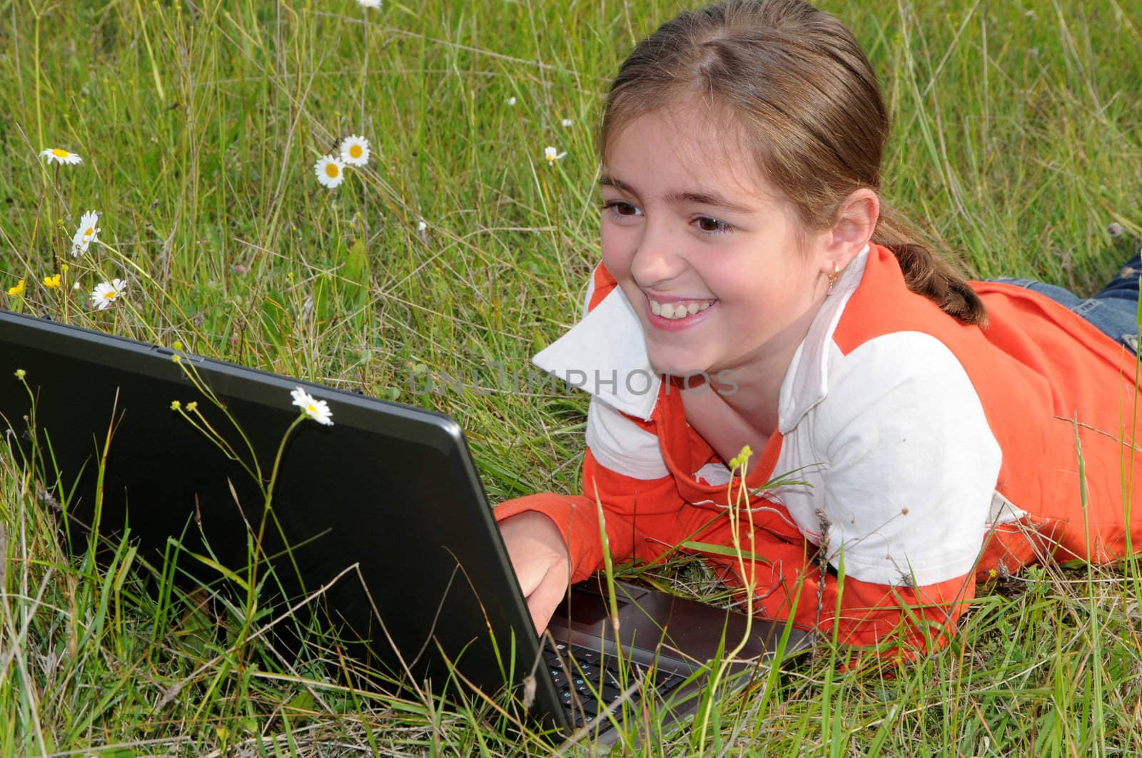 girl lies on a grass on to the meadow and works with a notebook