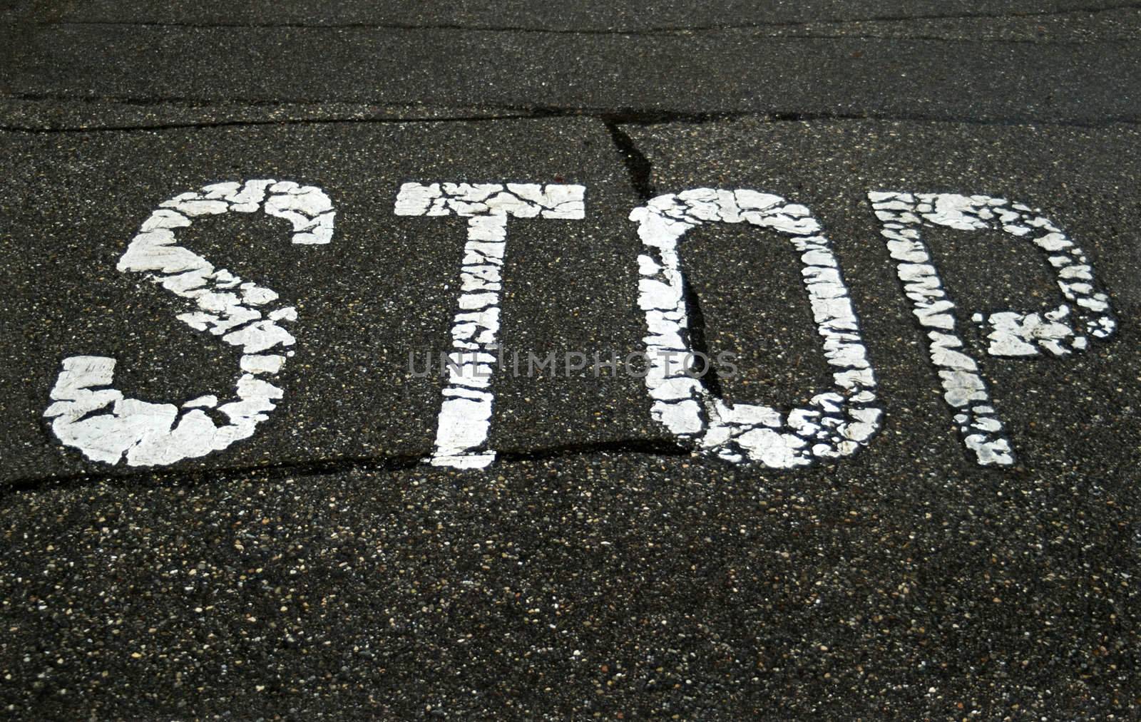 A very old stop sign at a road junction. The road-paint is cracked and worn. The tarmac is wet as it was raining when this photograph was taken.