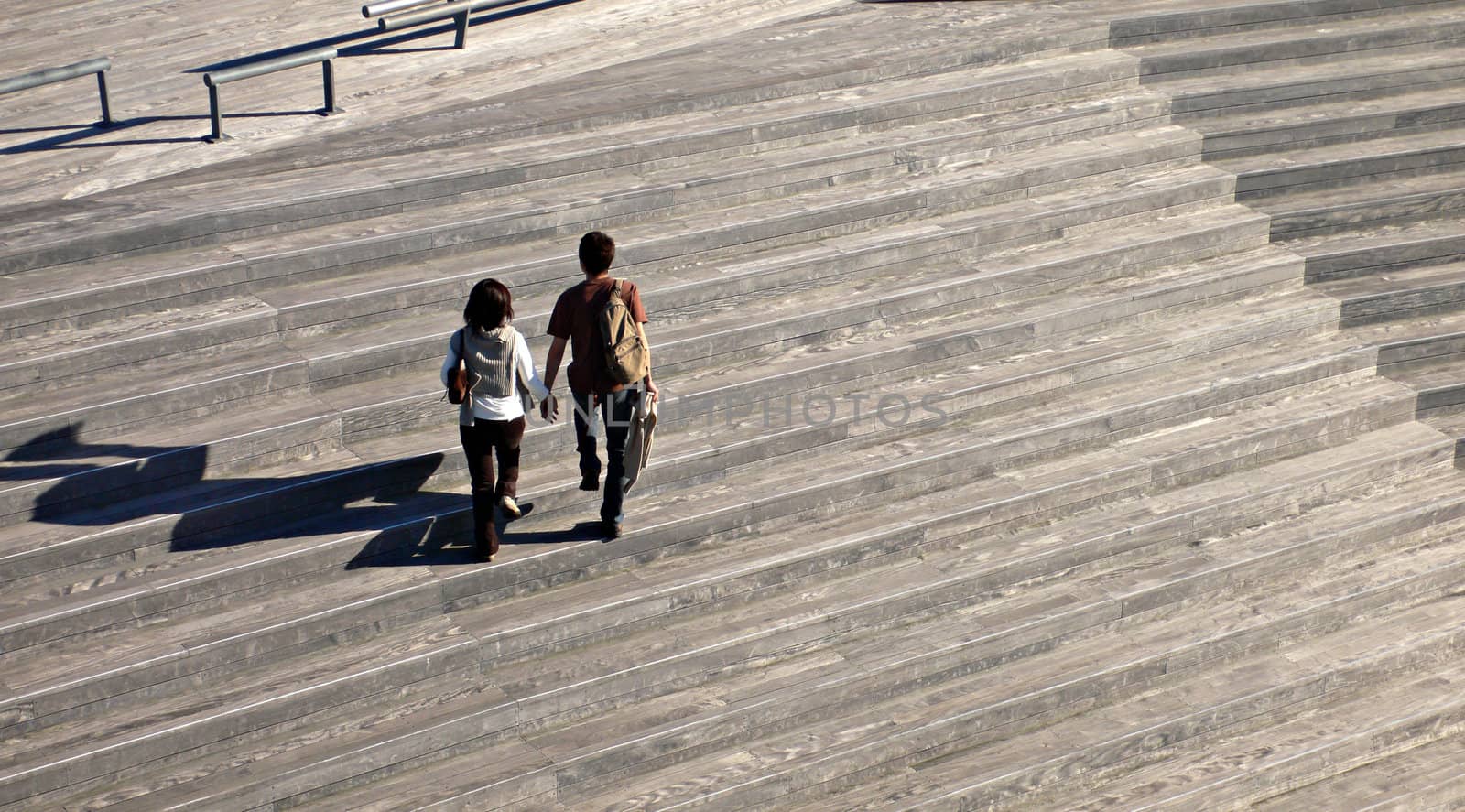 two peoples with long shadows walking on the wooden stairs
