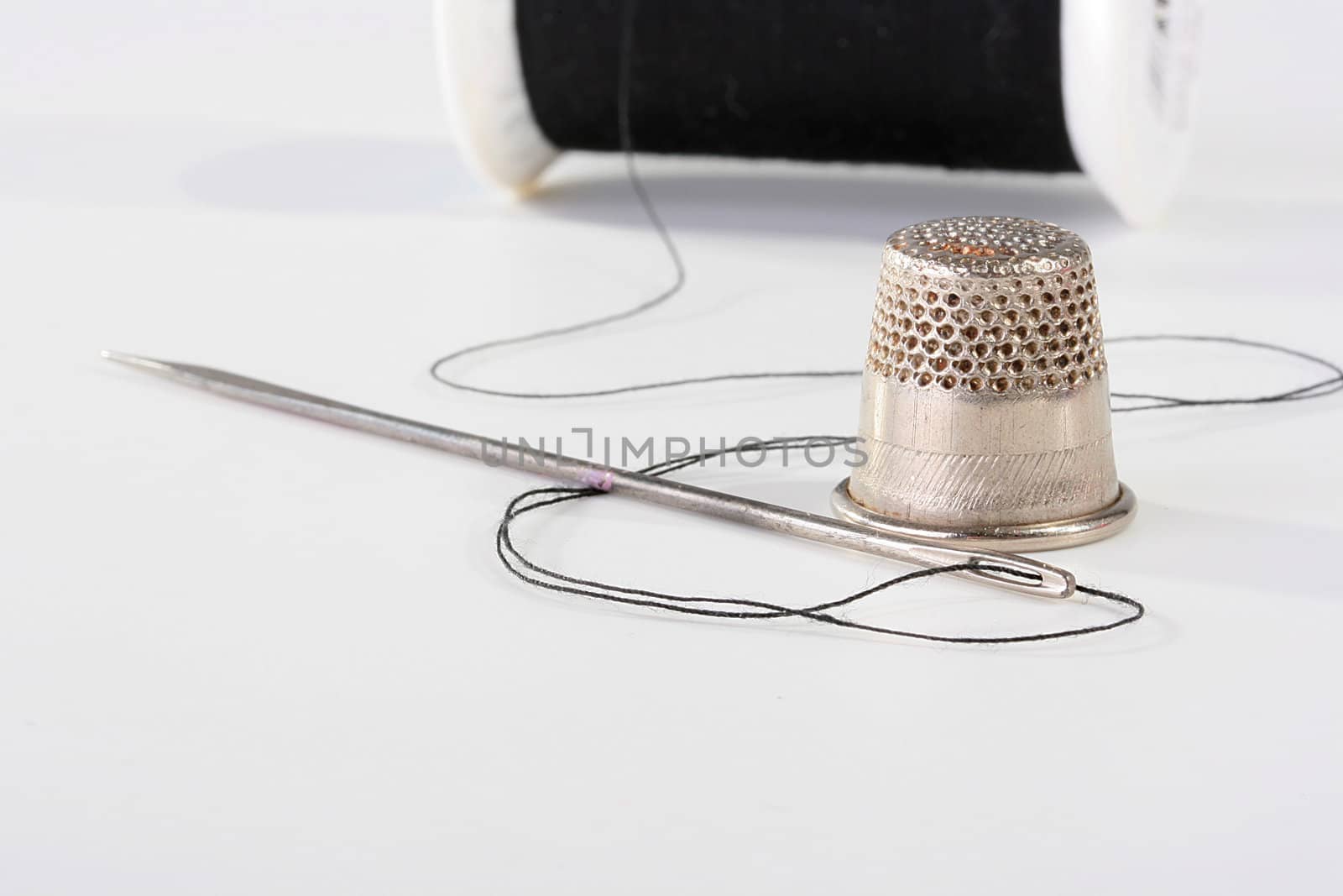 The needle with a black thread is connected to the coil, the thimble nearby lies.