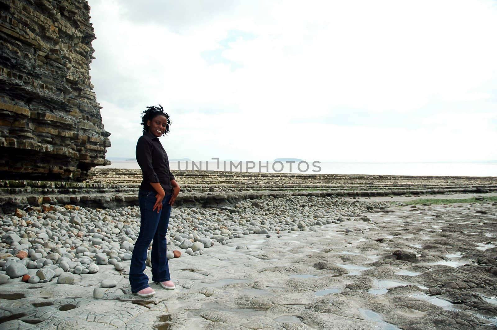 african girl in front of rock lat the beach, looking at the sea