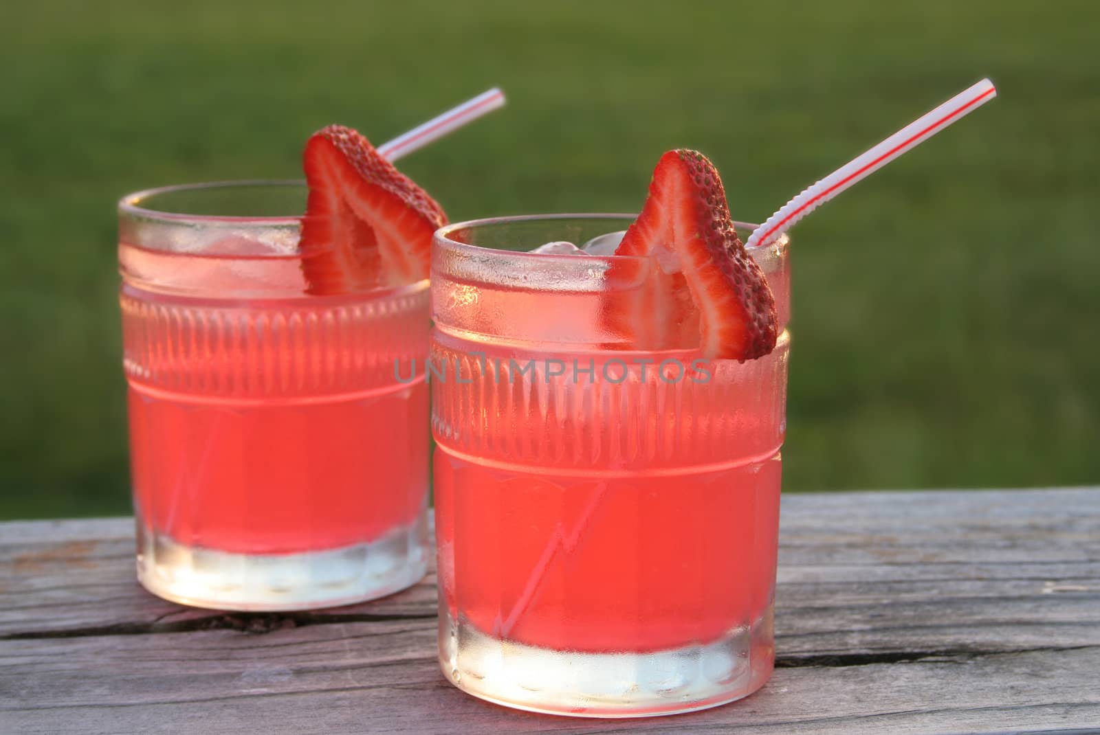two glasses of ice cold pink lemonade/or strawberry cocktail garnised with fresh sliced strawberries.