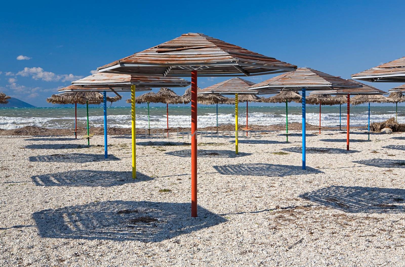 Set of beach umbrellas on sand making shadows under the blue clear sky in hot day
