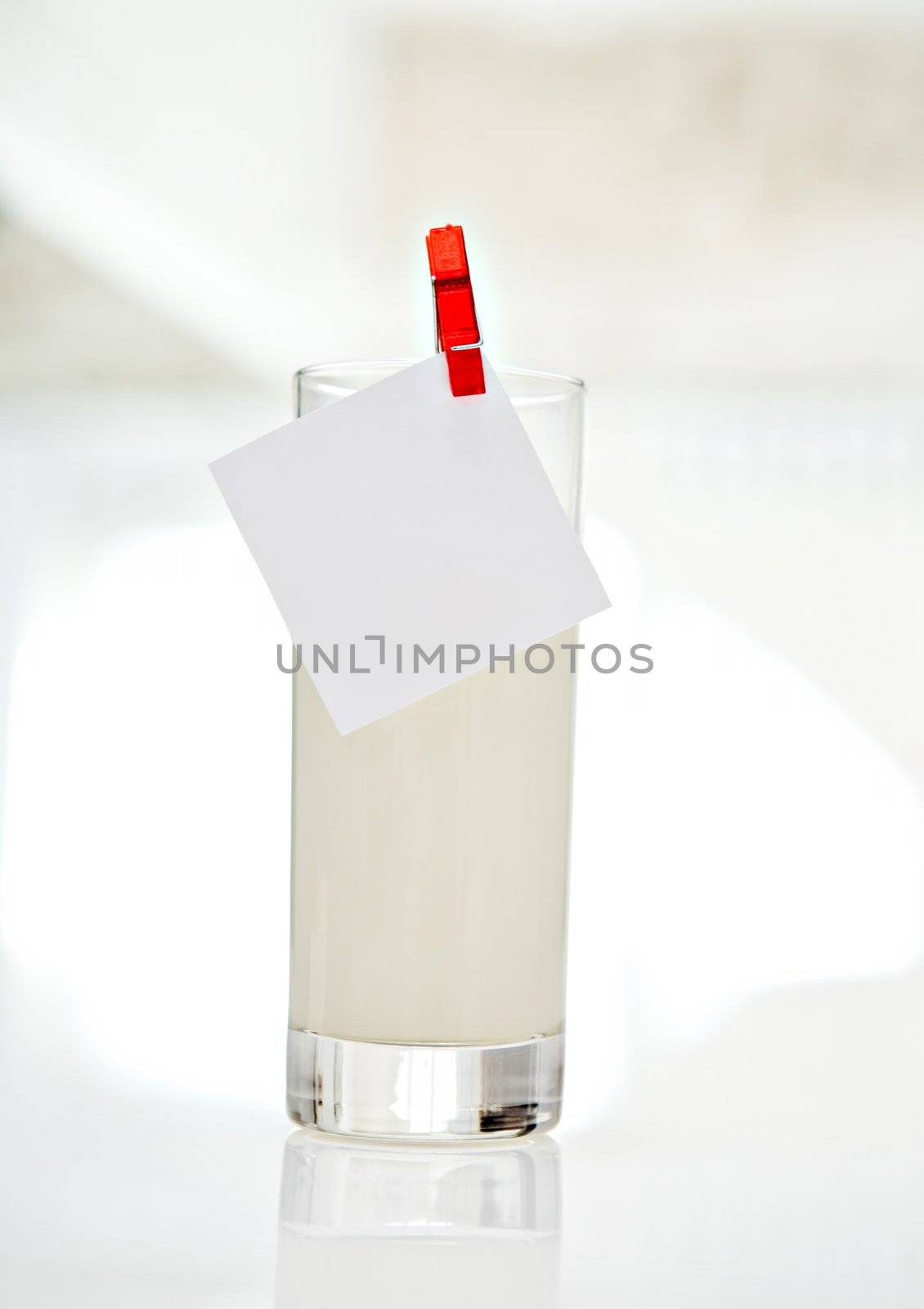 Note is attached to the glass of milk standing on a white table
