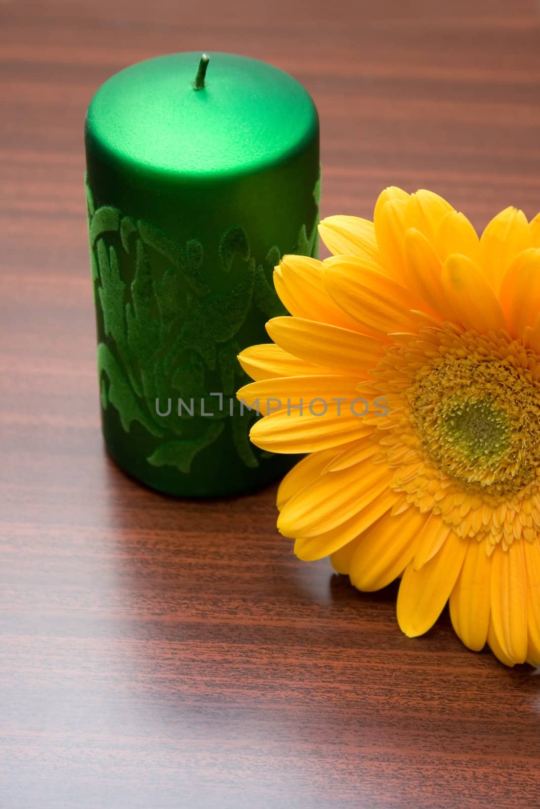 Yellow flower and green candle on wooden table