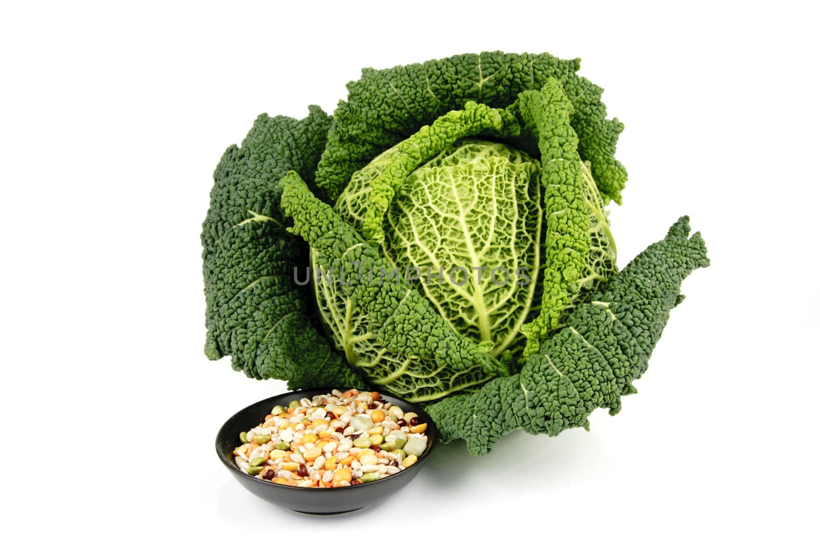 Single fresh ripe green cabbage and soup pulses in a small black dish on a reflective white background 