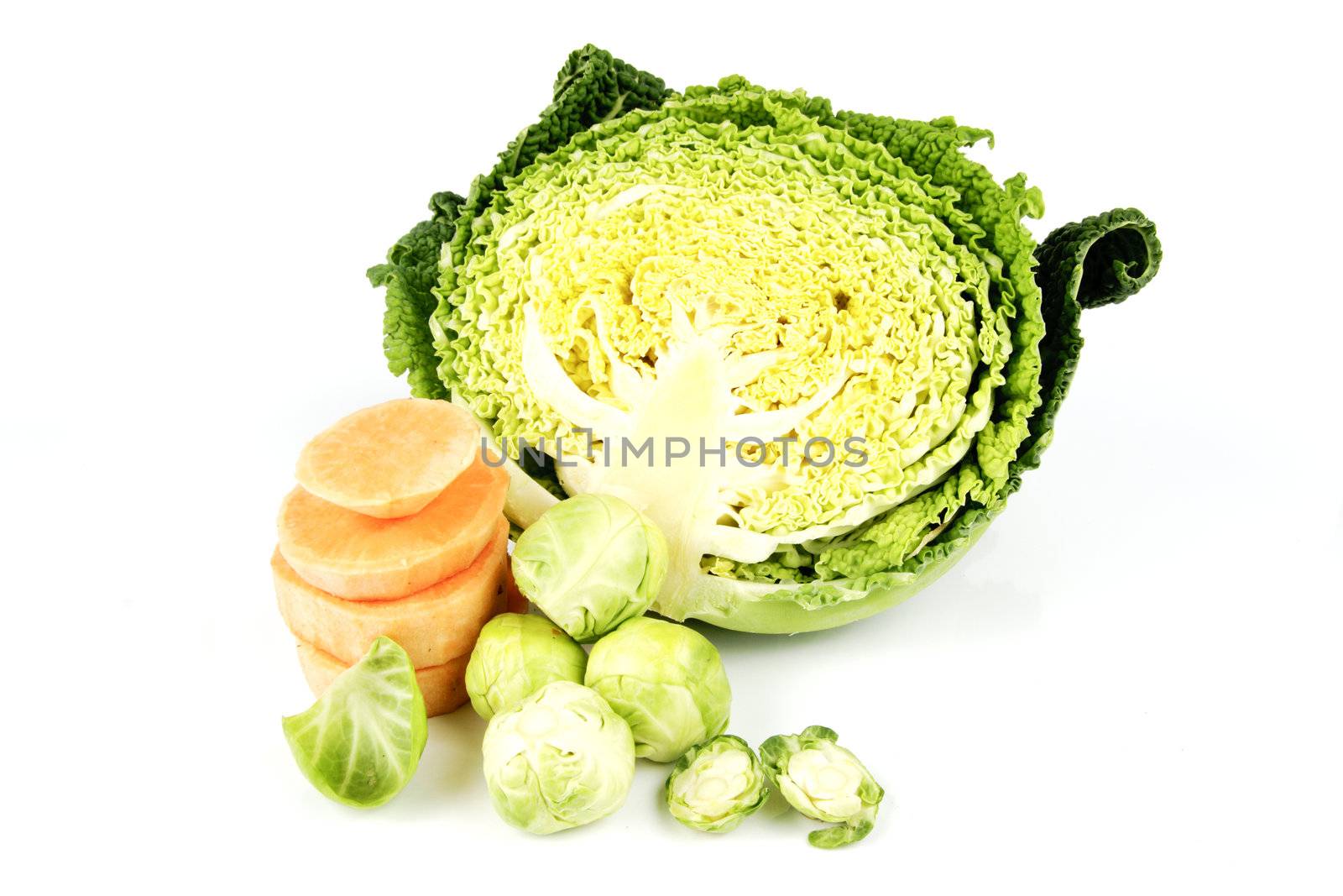Half a raw green cabbage with slices of raw sweet potato and peeled green sprouts on a reflective white background