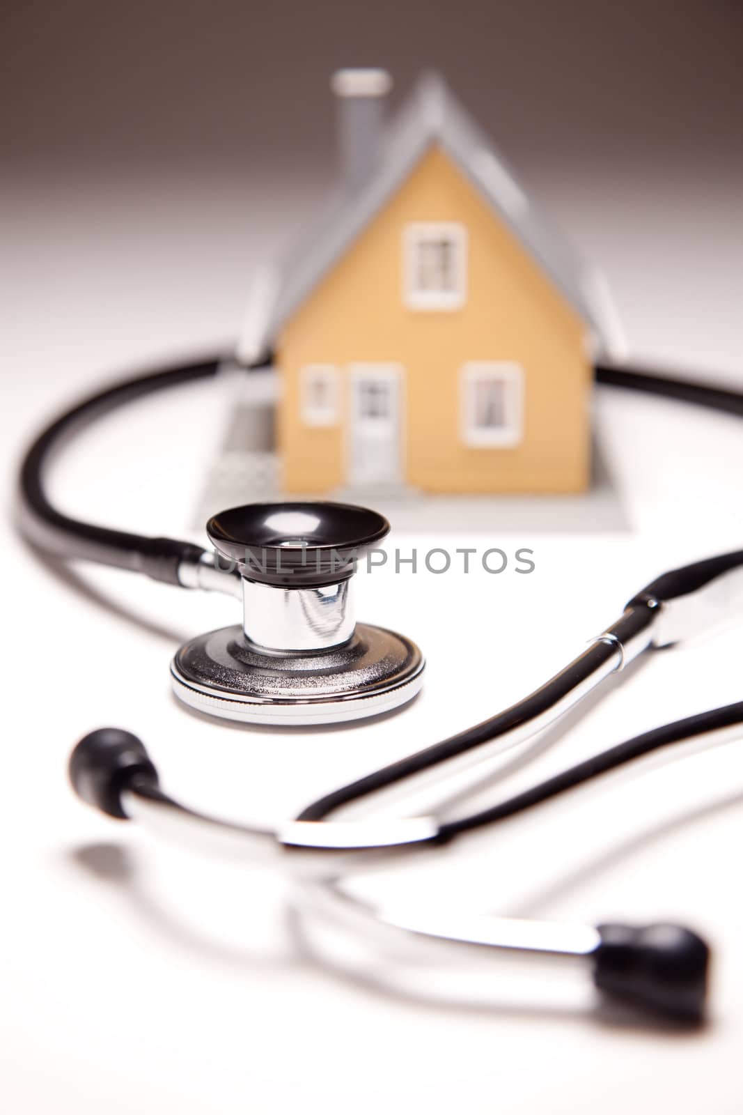 Stethoscope and Model House on Gradated Background with Selective Focus.