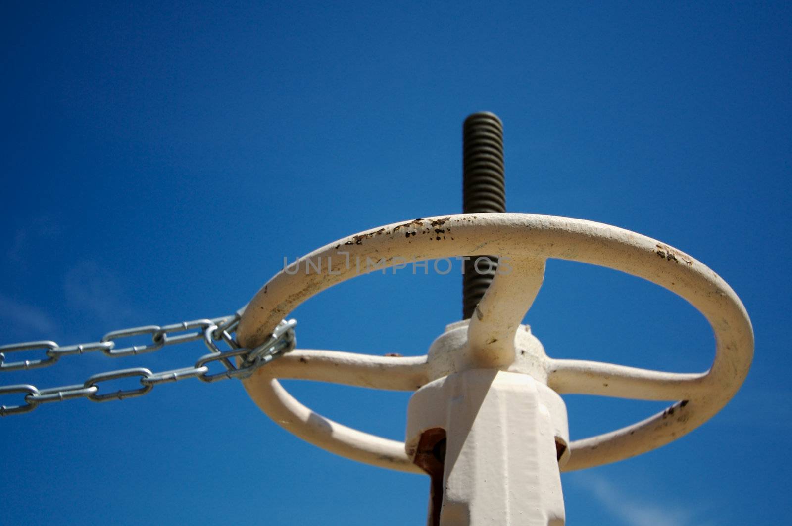 Industrial Valve & Chain Abainst A Deep Blue Sky.