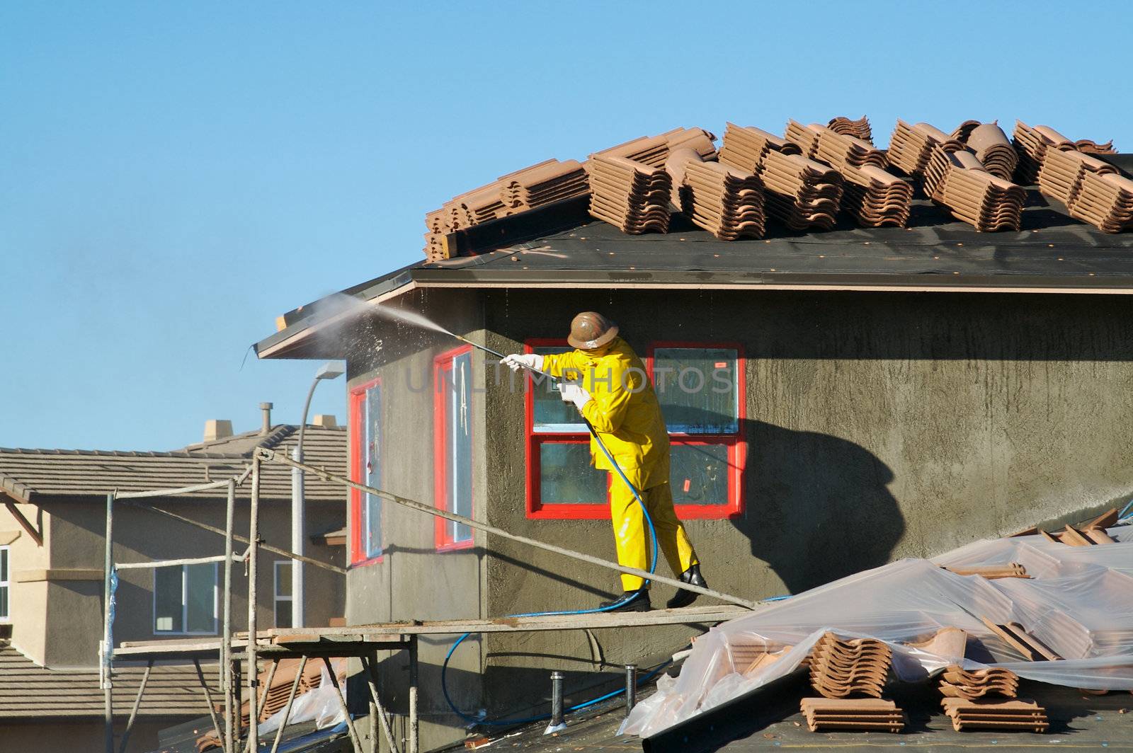 Construction worker pressure washes fresh applied surface of new home exterior.