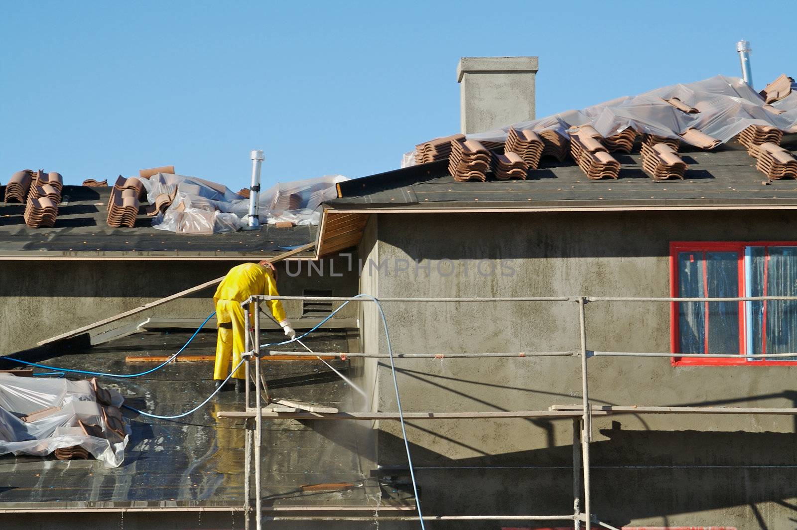 Construction worker pressure washes fresh applied surface of new home exterior.