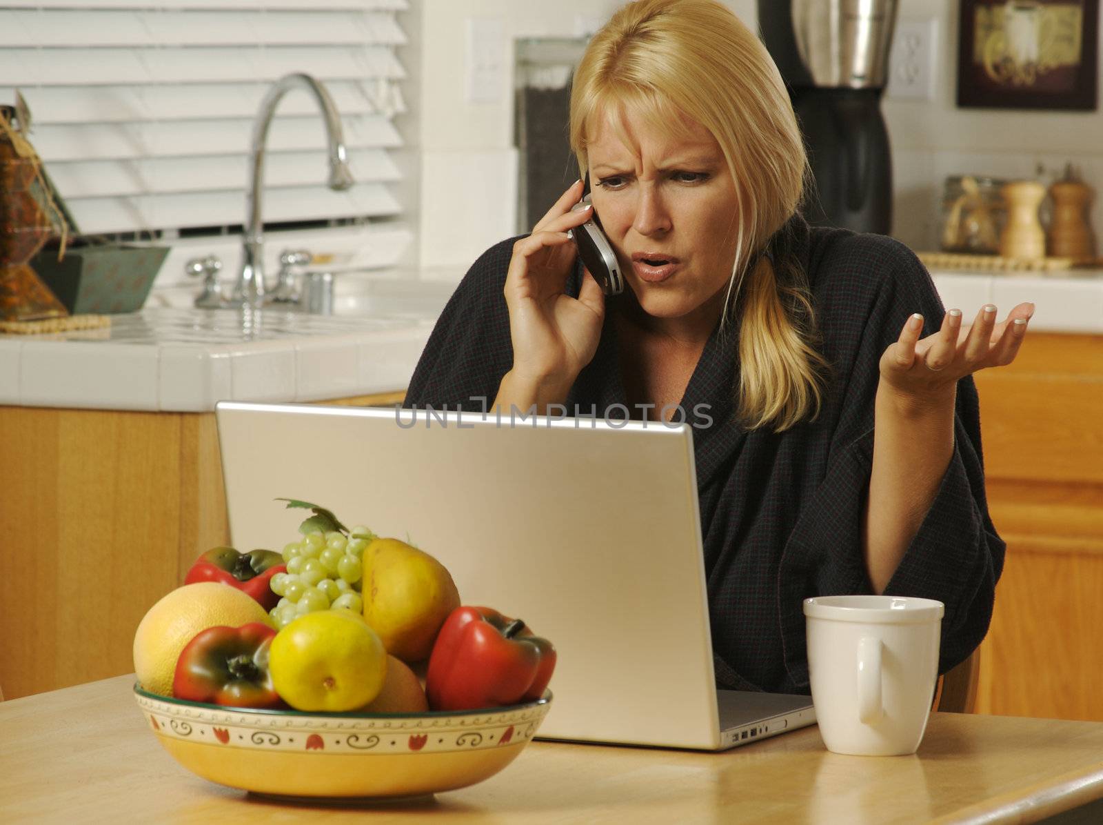 Woman in her kitchen on cell phone sitting in front of laptop. Computer problems?