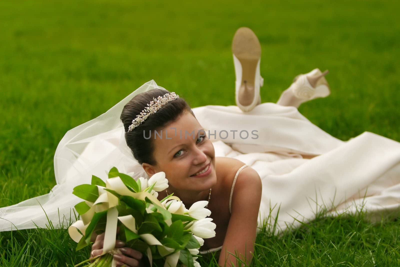 The beautiful bride with a wedding bouquet lays on a grass