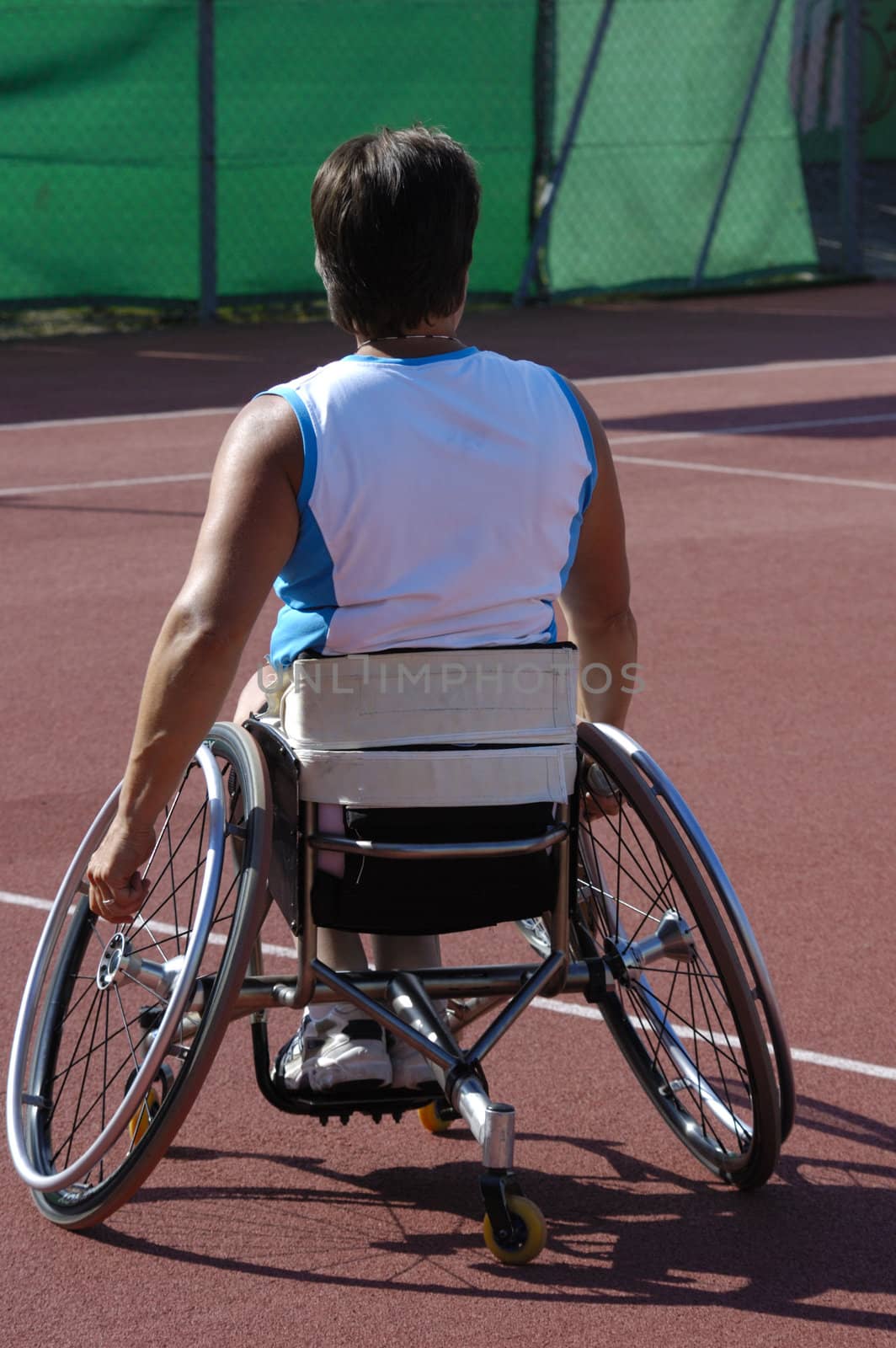 A wheelchair athlete taking a moment's pause during a tennis championship match. Her tennis racquet can just be seen in her right hand and a little sweat on the back of her blouse.