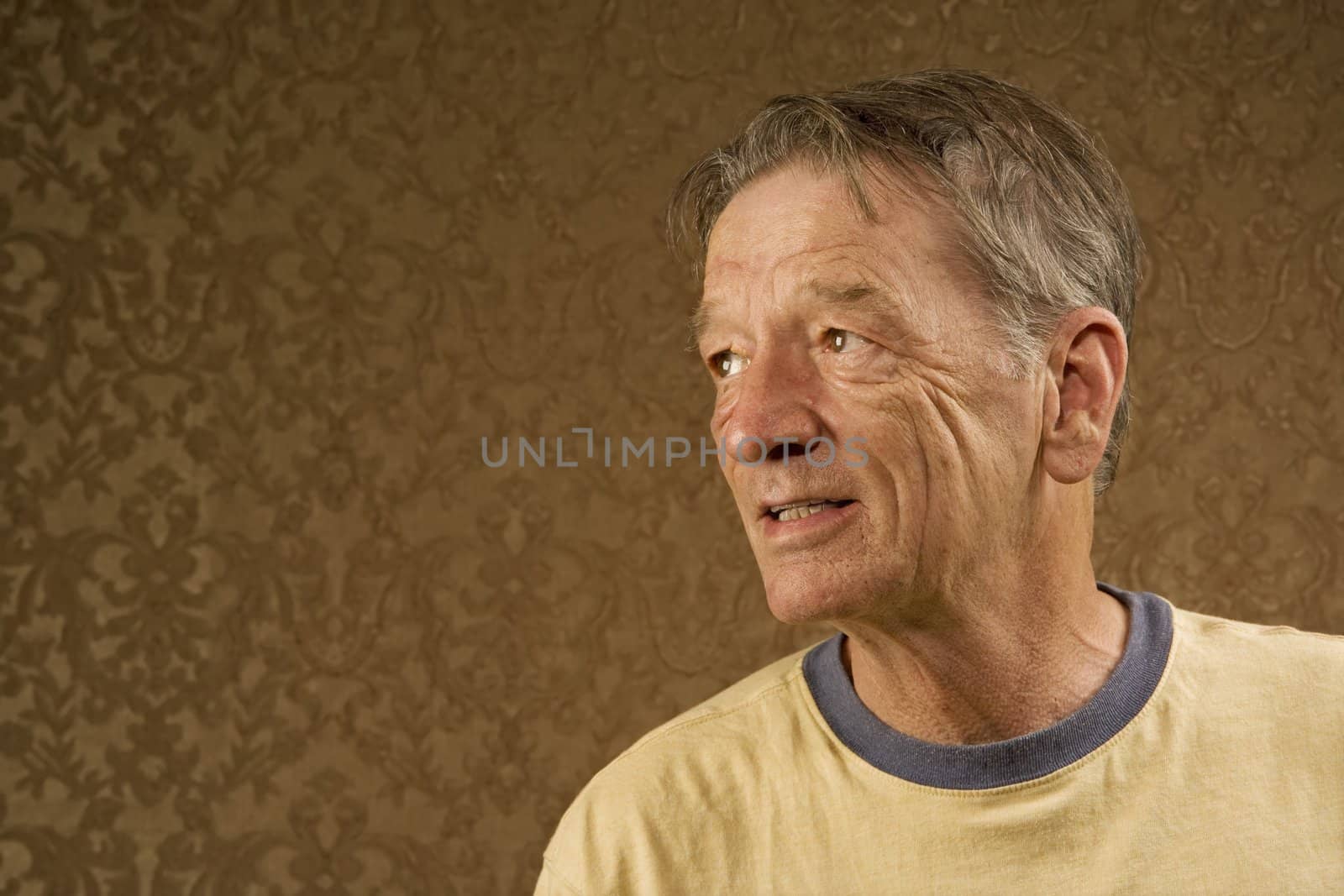 Man with a craggy face wearing a yellow shirt against a gold background with copy space