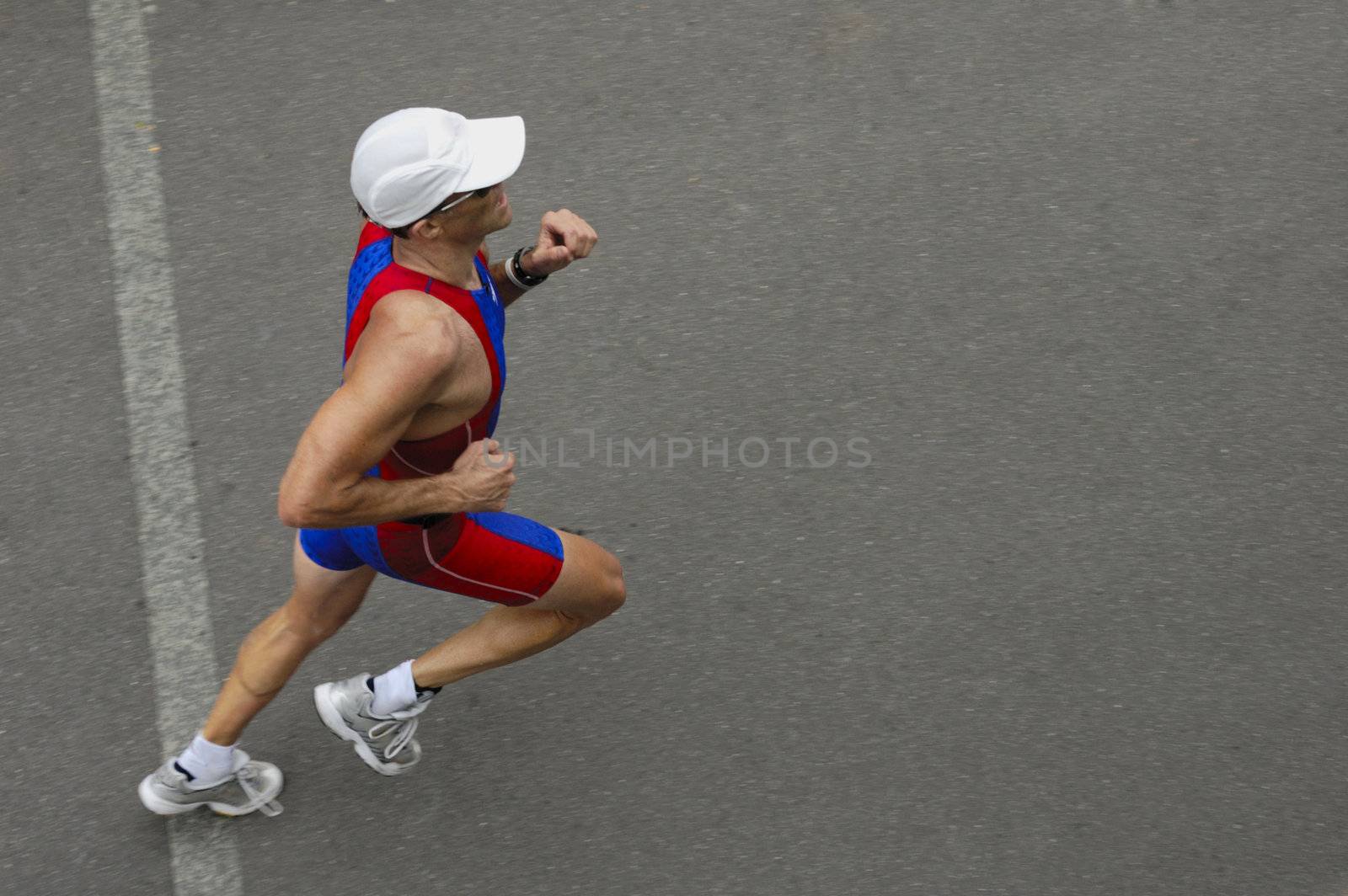 A marathon runner crossing a line, taken from above. Motion blur on his feet. Space for text on the tarmac in front of him.