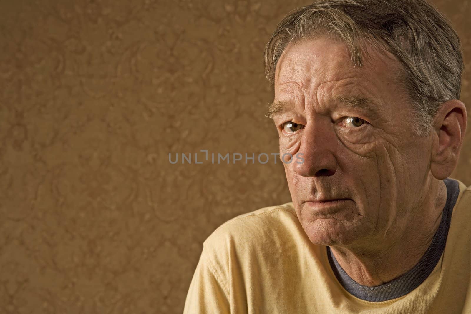 Man with a craggy face wearing a yellow shirt against a gold background with copy space