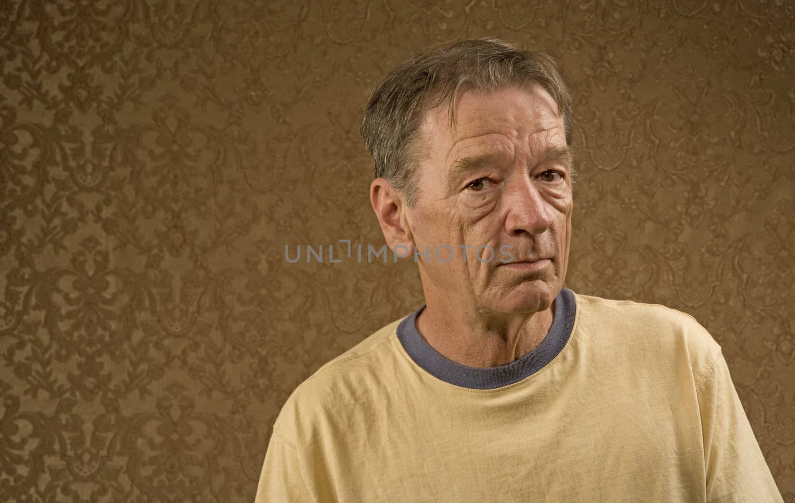 Man with a craggy face wearing a yellow shirt against a gold background with copy space