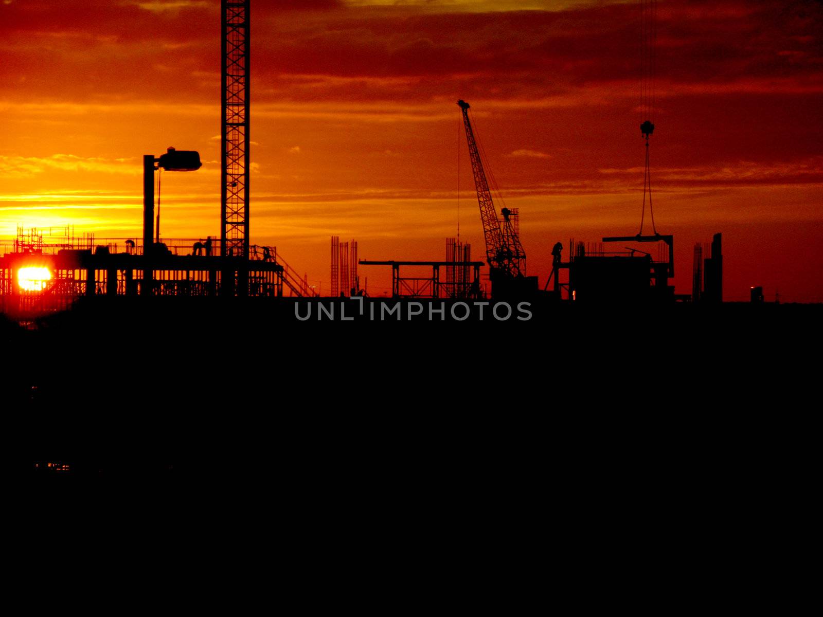 Cranes and construction site silhouette against setting (or rising) sun