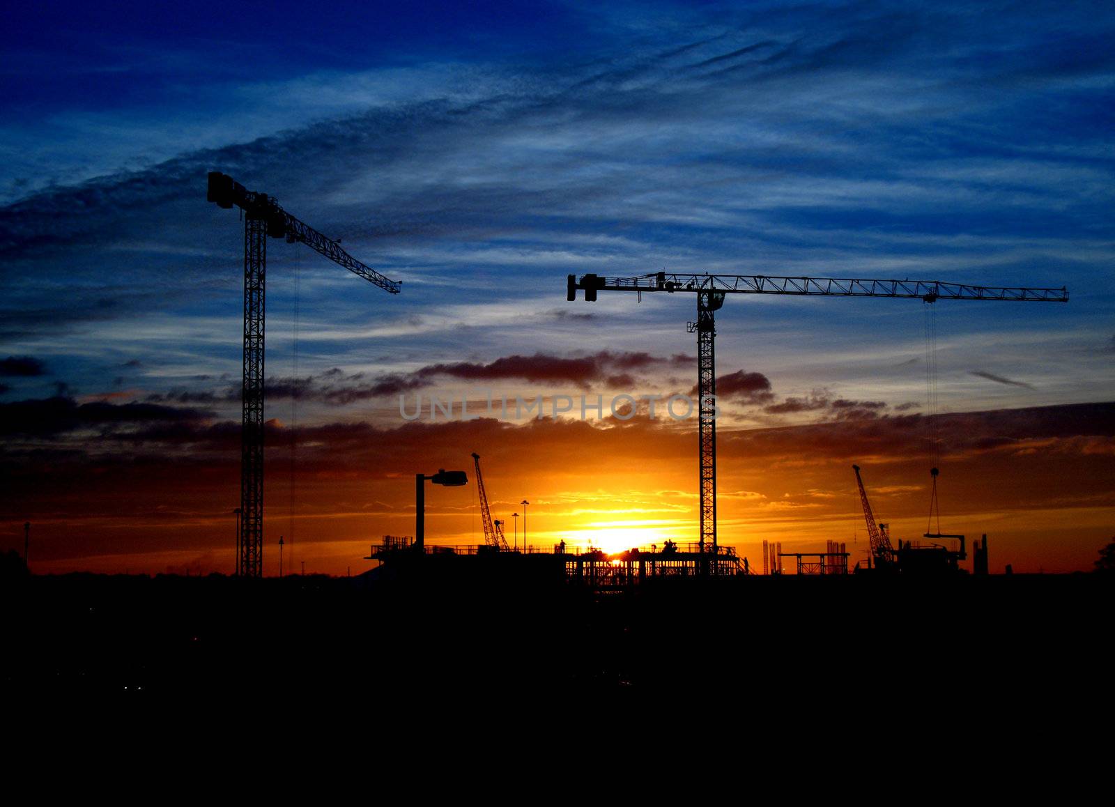 Cranes and construction site silhouette against setting (or rising) sun