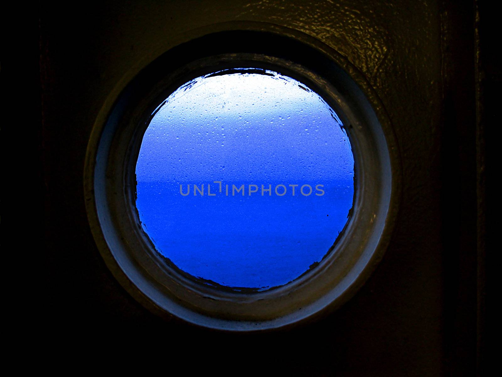 View out of a rainy porthole looking at a blue sky and horizon