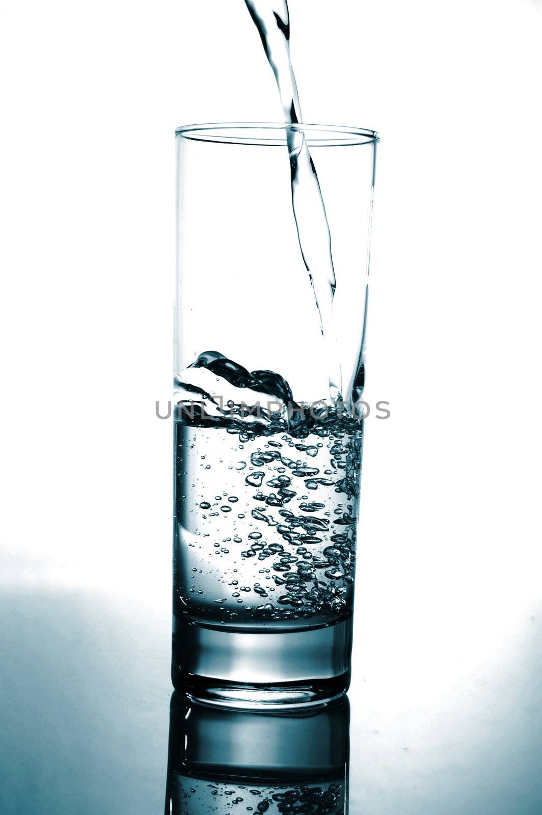 glass with pouring water with reflection on white