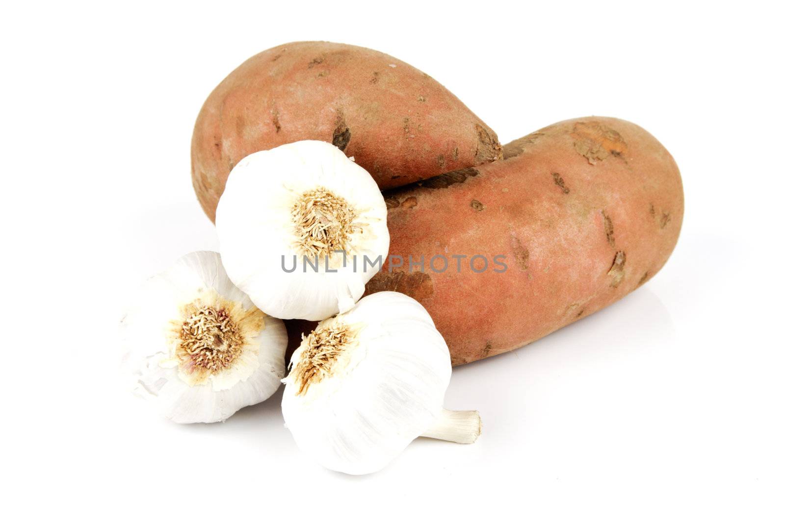 Two raw unpeeled sweet potatoes with white garlic bulbs on a reflective white background