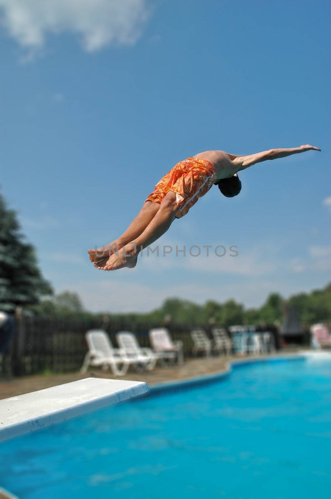 A boy does a dive off of a diving board at a home swimming pool of blue water.