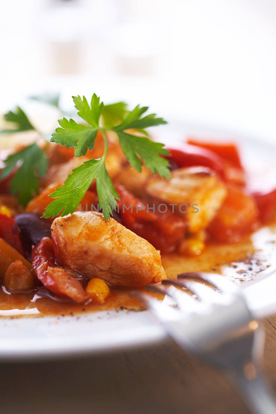 Focus on the plate of goulash with green parsley on it and fork on napkin beside it.