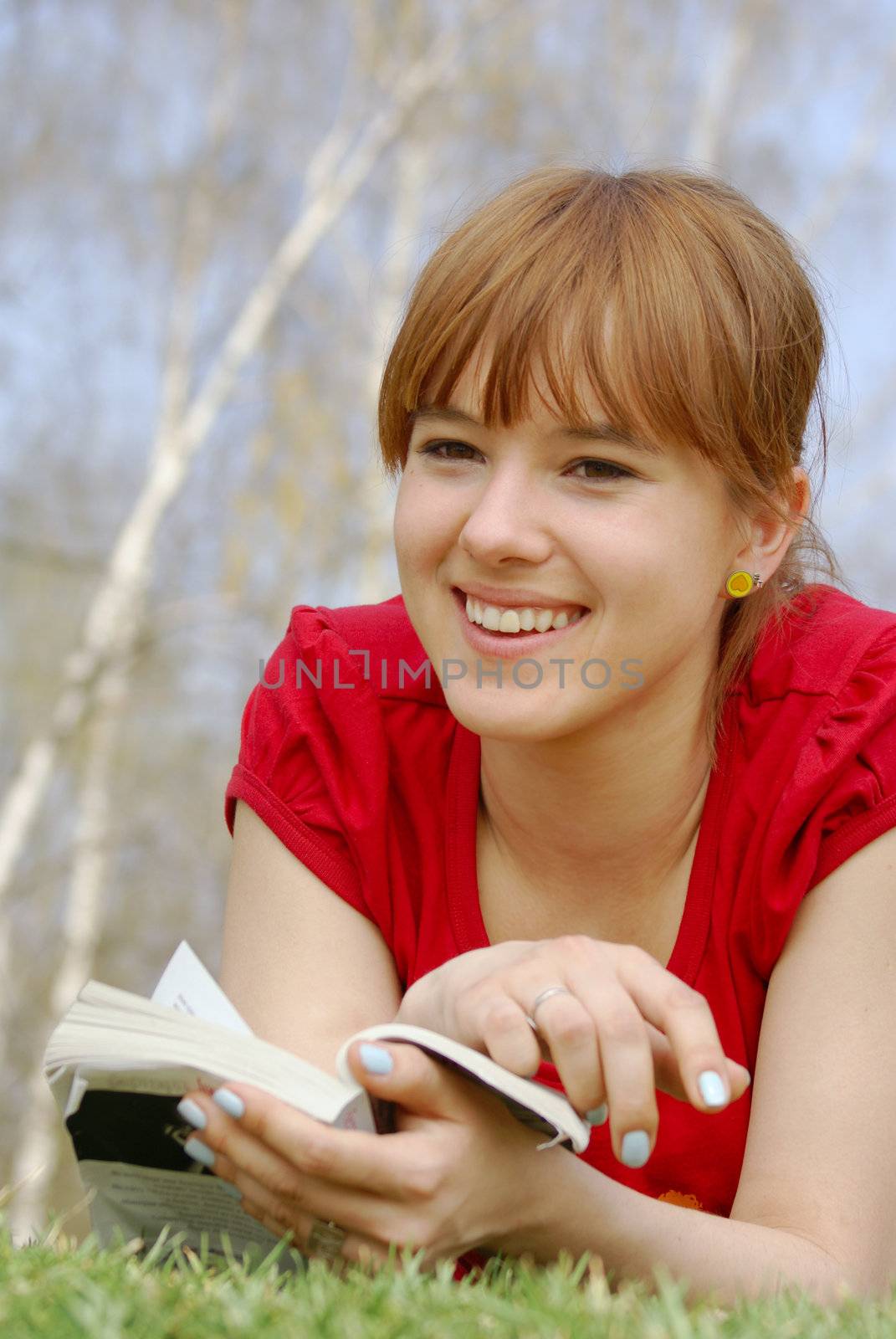 Young girl lying with a book on spring grass in a park and smiling