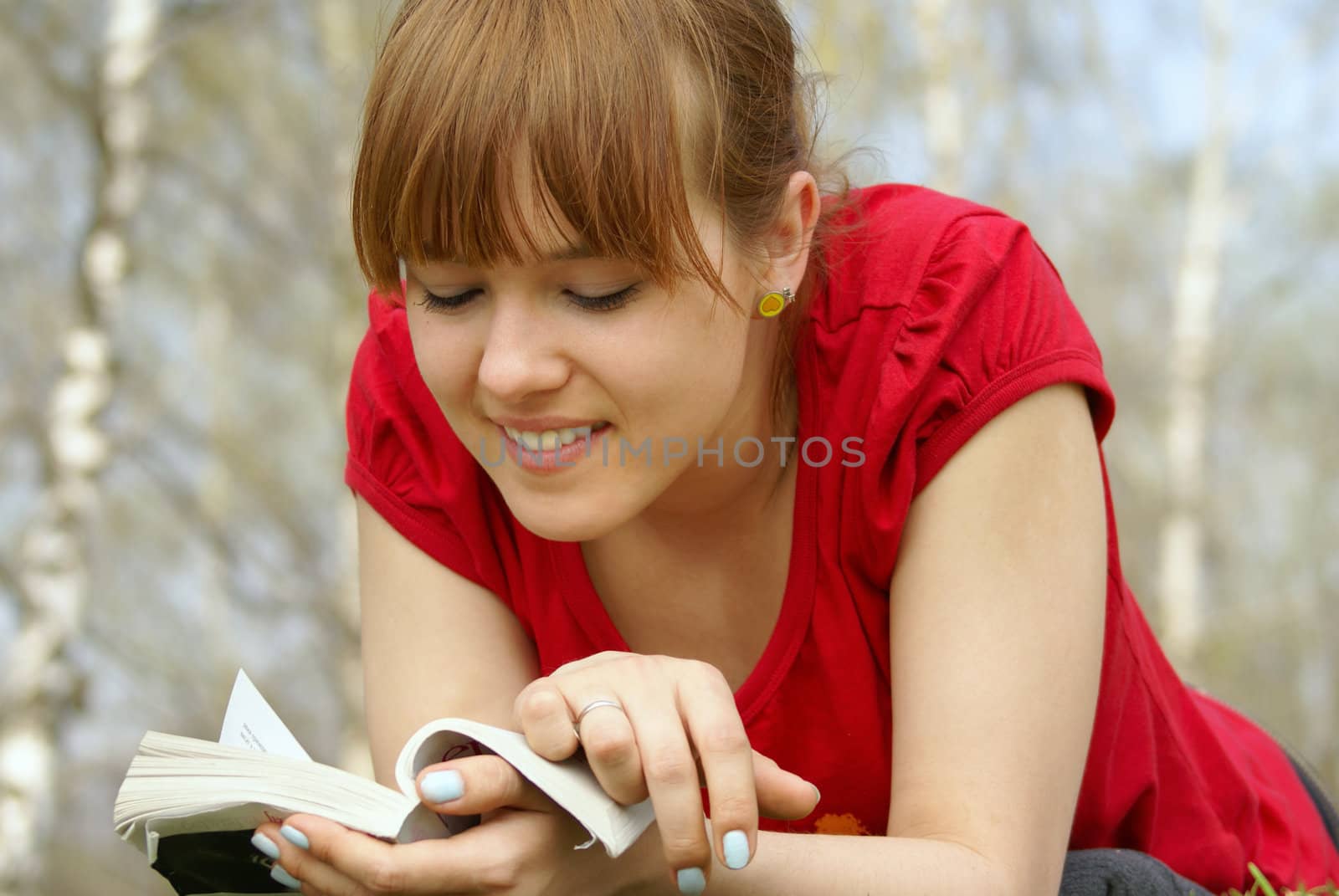 Young girl lying with a book on spring grass in a park and reading