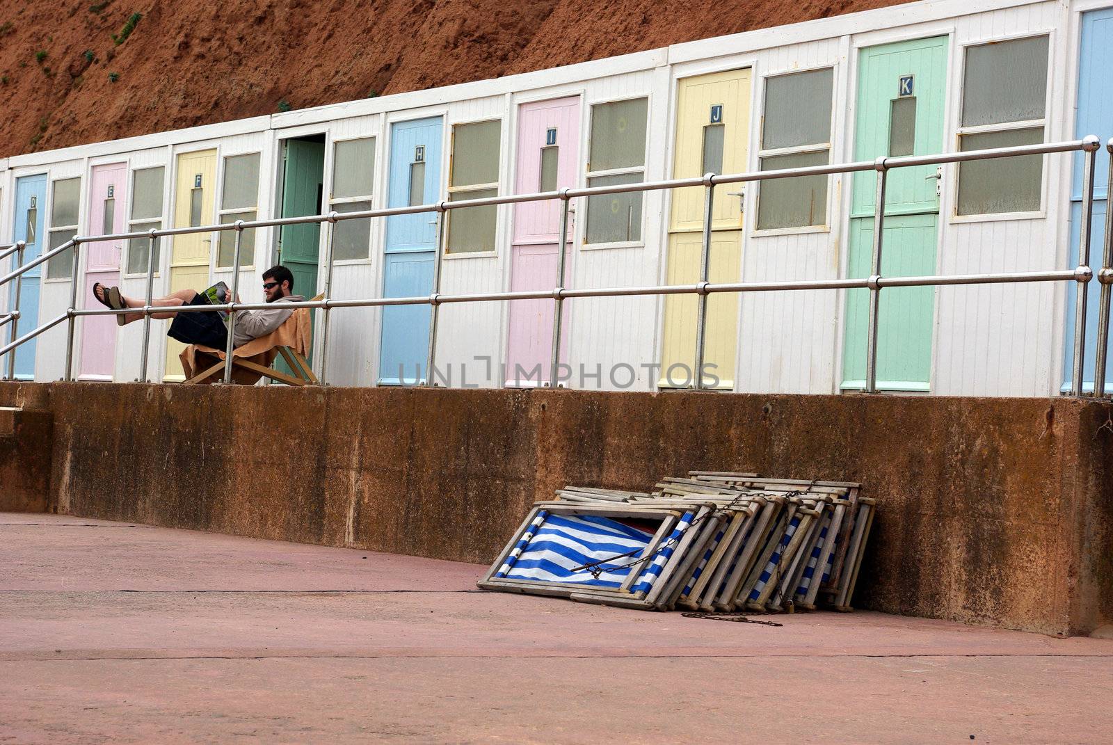 Photo of a man reading and relax on the seaside in front of beach cabins