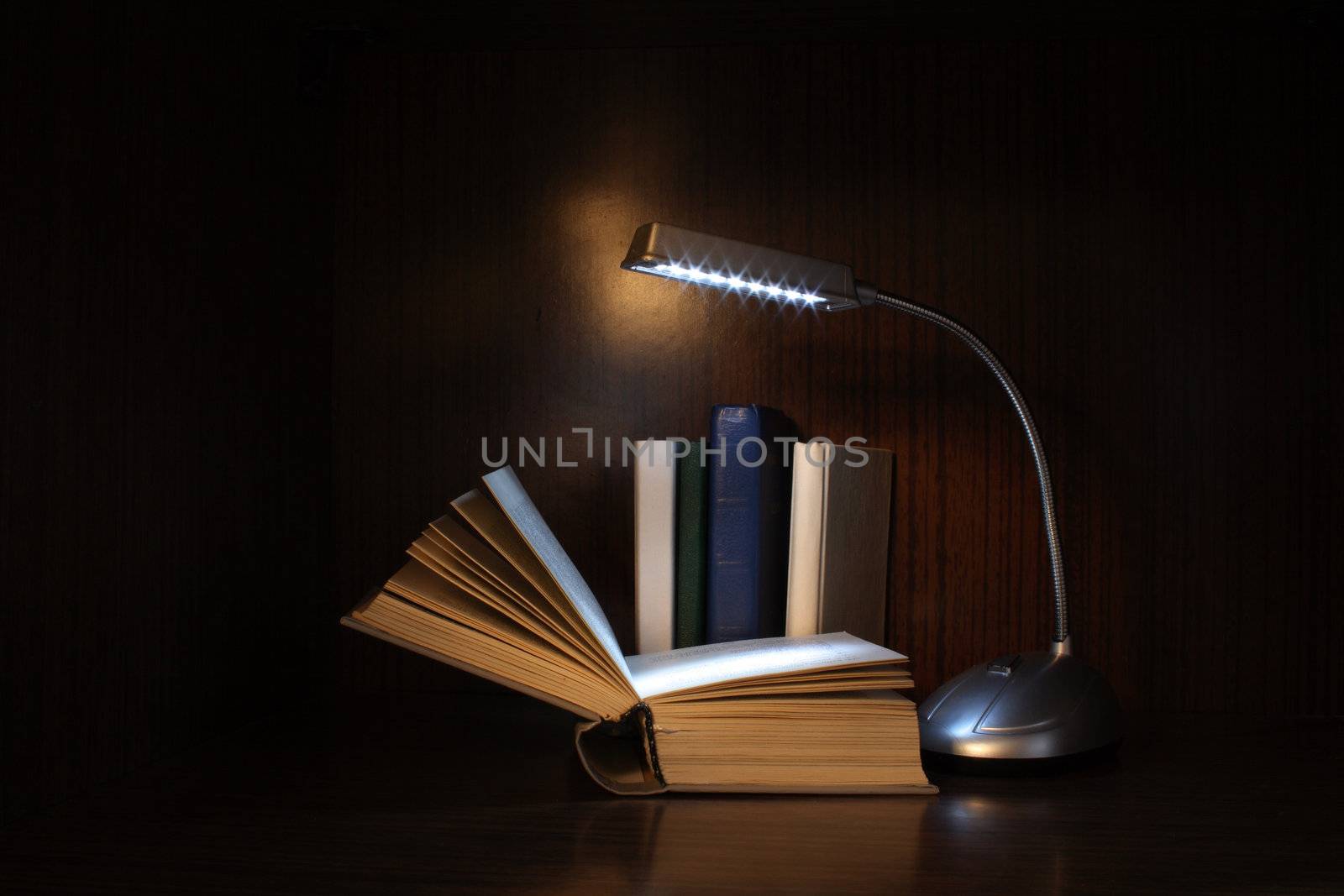 Books and lighting reading lamp on dark background