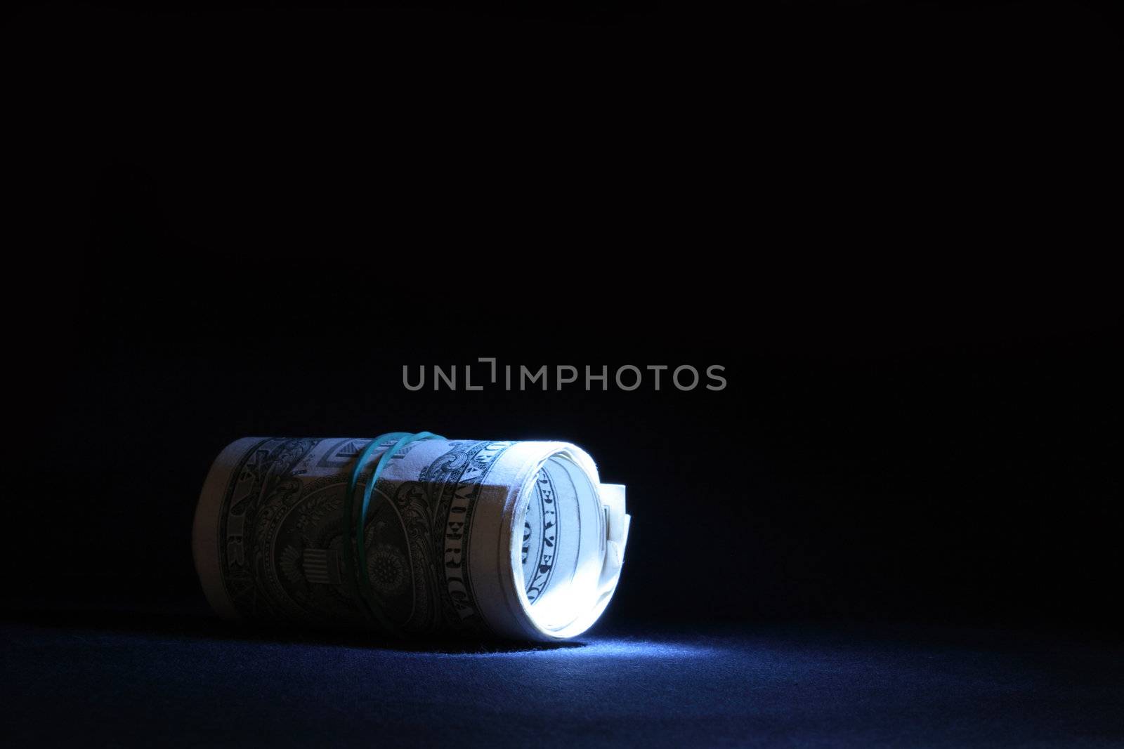 Little roll of dollar banknotes lying on dark background