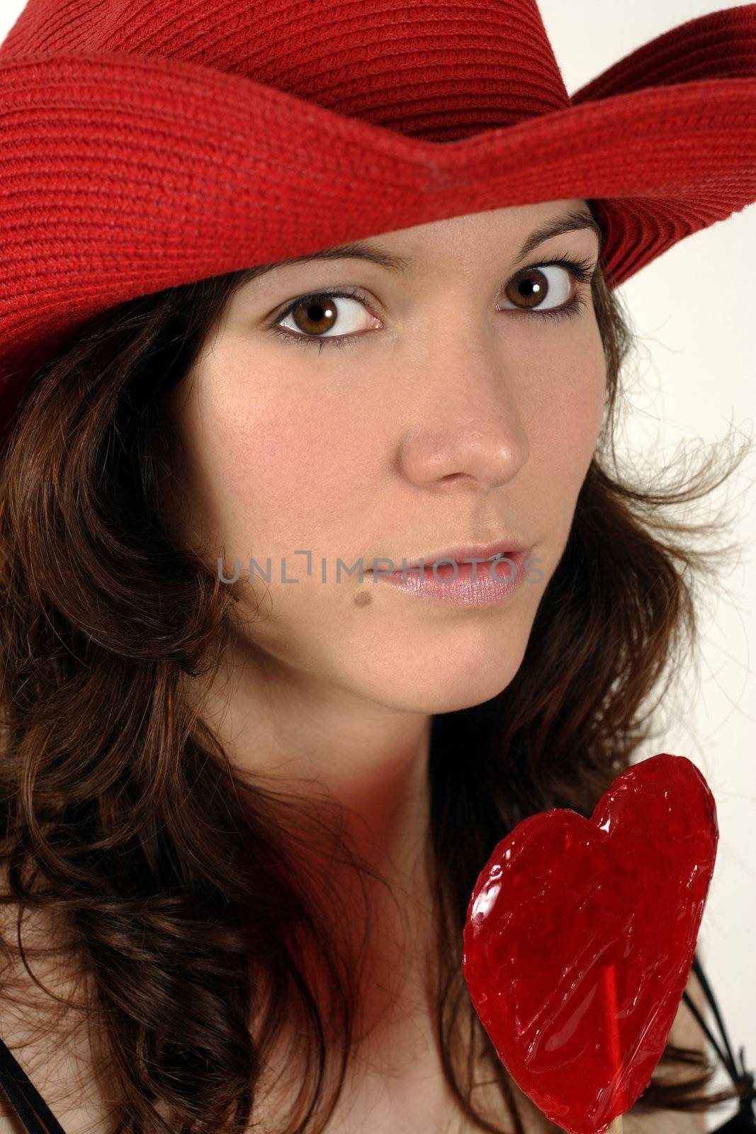 Image of a beautiful young woman wearing a red cowboy and holding a heart-shaped lollipop.
