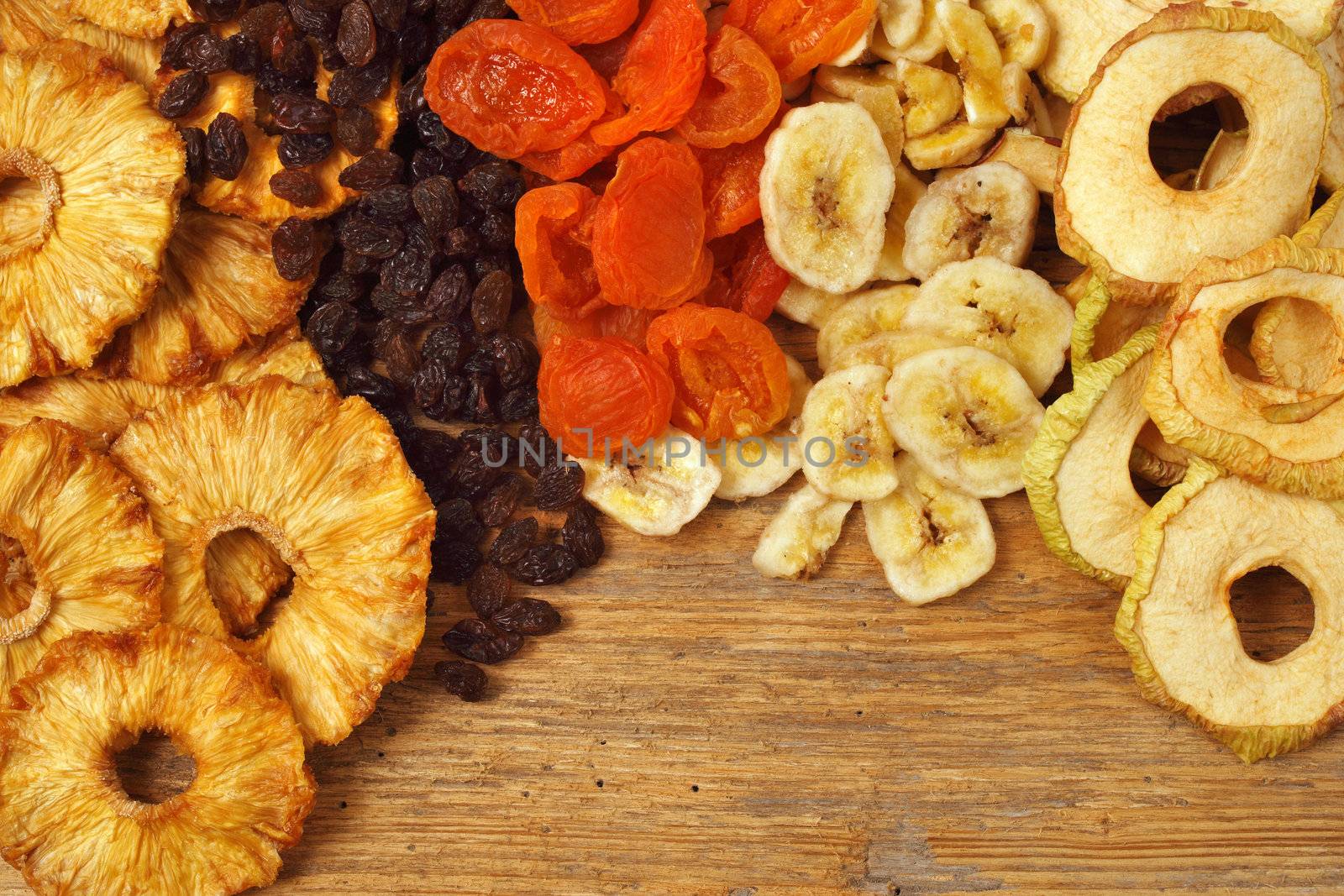 Various dried fruit displayed on an old wooden table - apple rings, pineapple rings, apricots, raisins, and banana slices.

