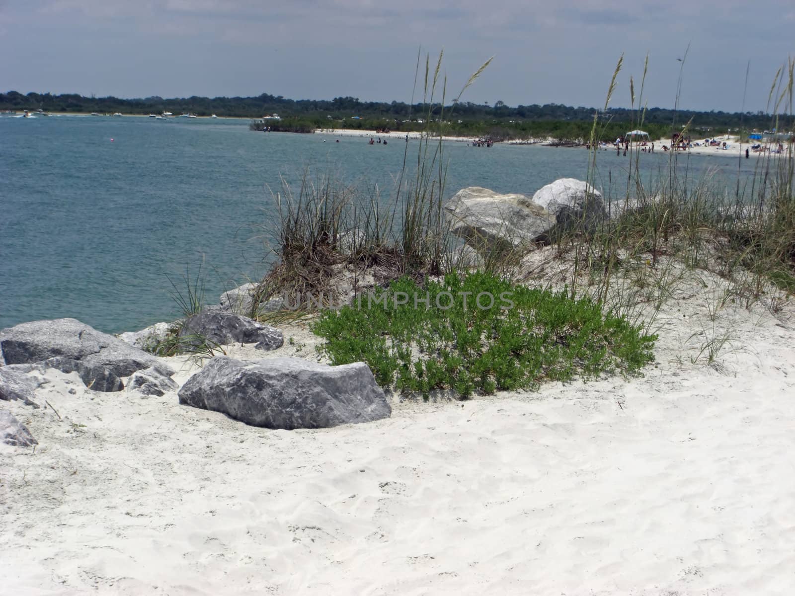 On top of the dunes at the edge of an ocean, lie some big rocks.