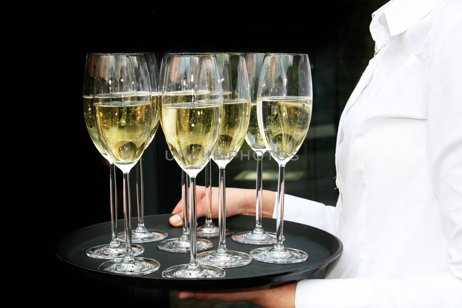 A waiter with champagne glasses on a tray. The background is black