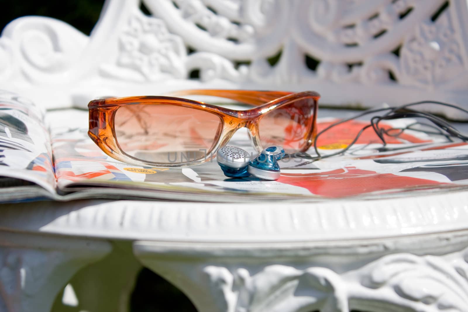 Sunglasses earphones and magazine left on a sunchair.