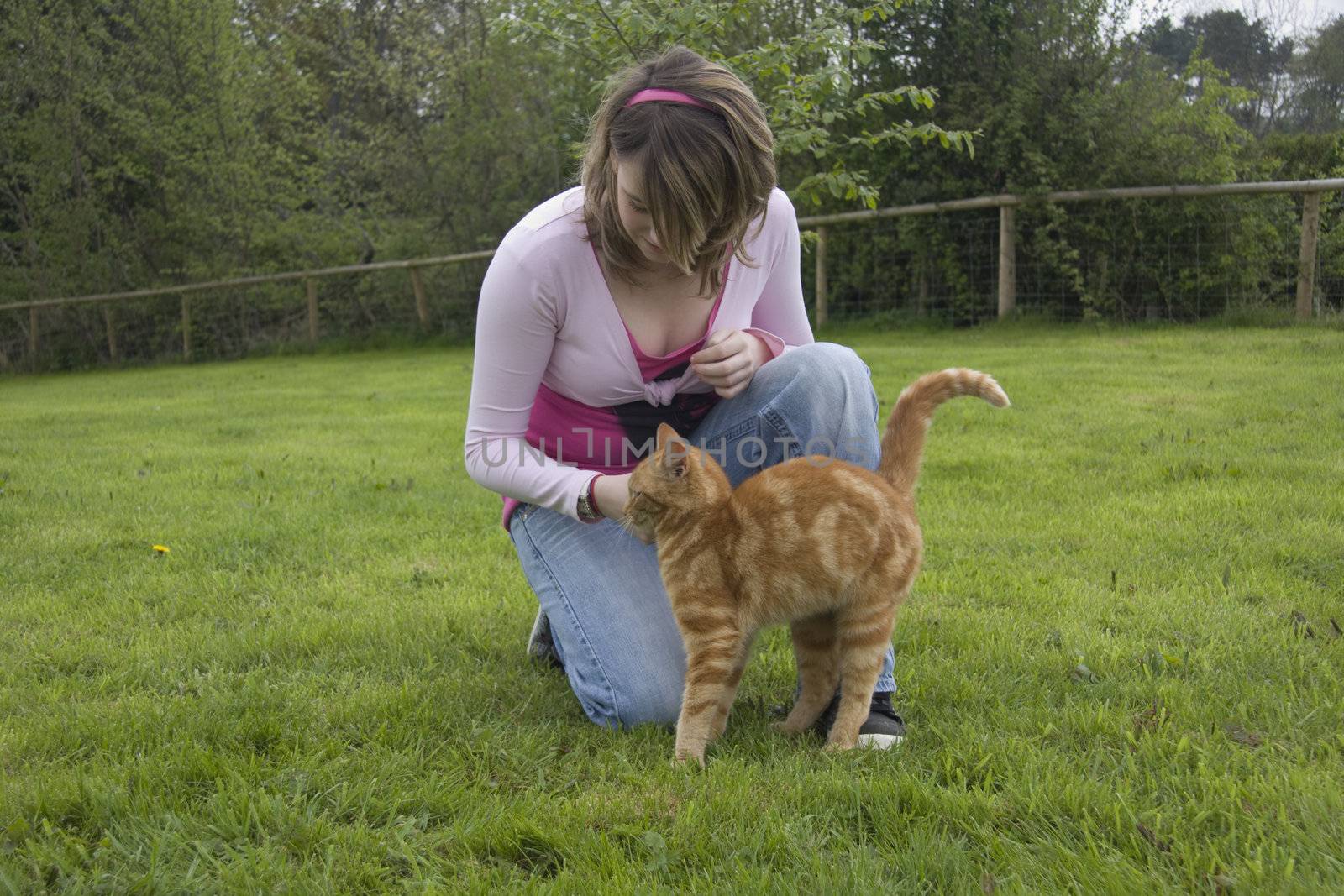 Pretty teenage girl strokes her ginger cat.