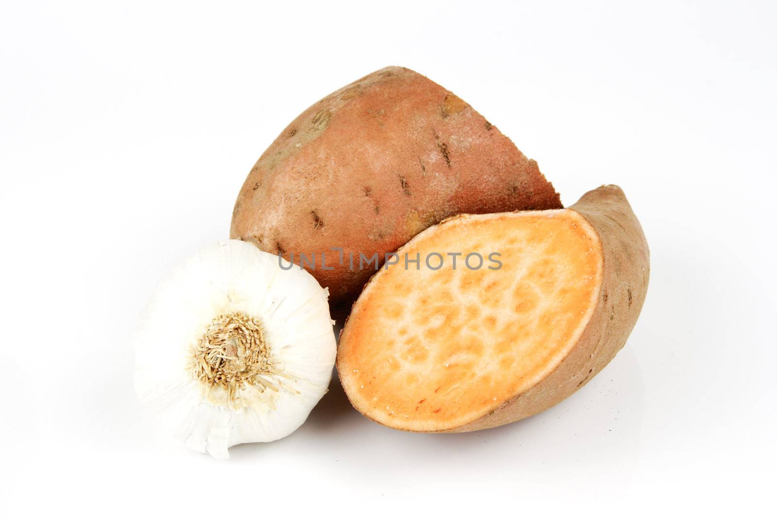 Sweet Potato cut in half with a white garlic bulb on a reflective white background