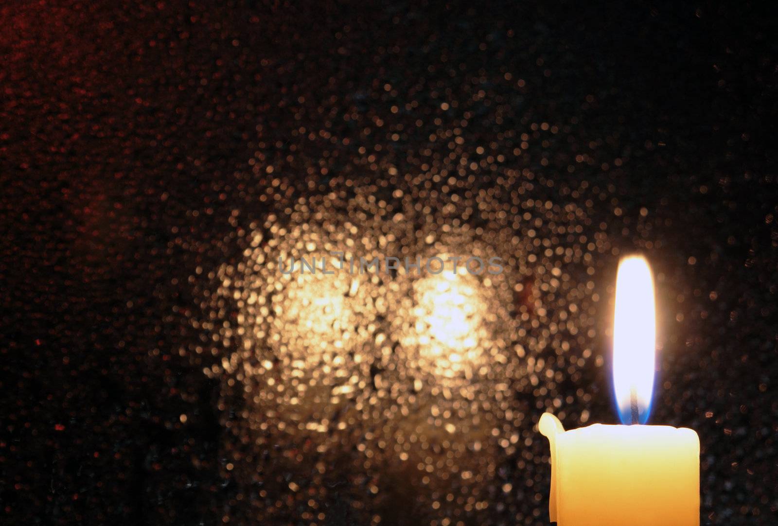 Candle with burning flame on dark glass background with reverberation